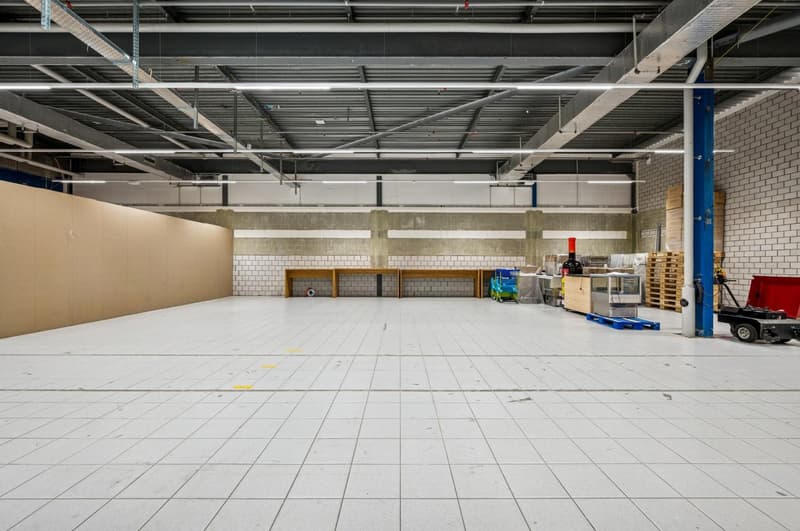 Open warehouse space, white tile floor, high ceiling, storage shelves, pallet racks, movable machinery