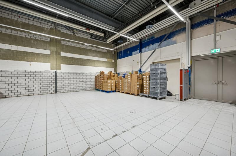 Wide, open storage space with tile flooring, brick walls, large piles of boxes, two gray double doors, gray storage units.