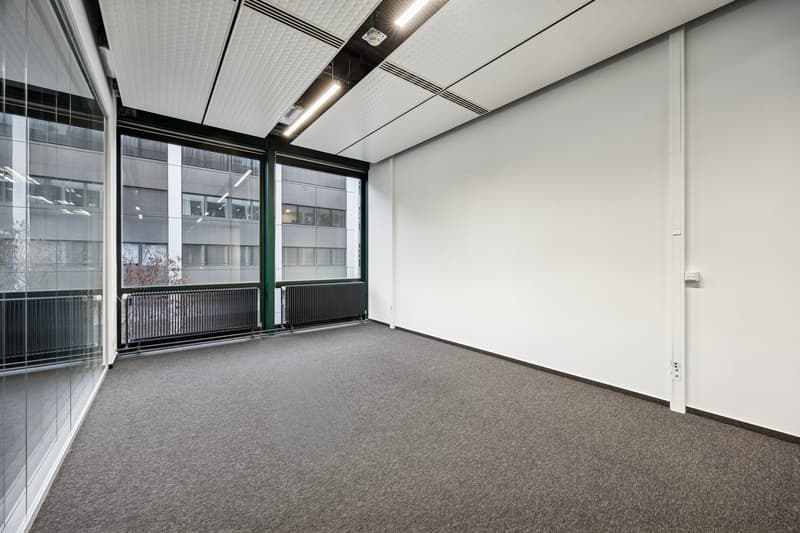 An empty room with glass windows, radiators, and carpeted floor.