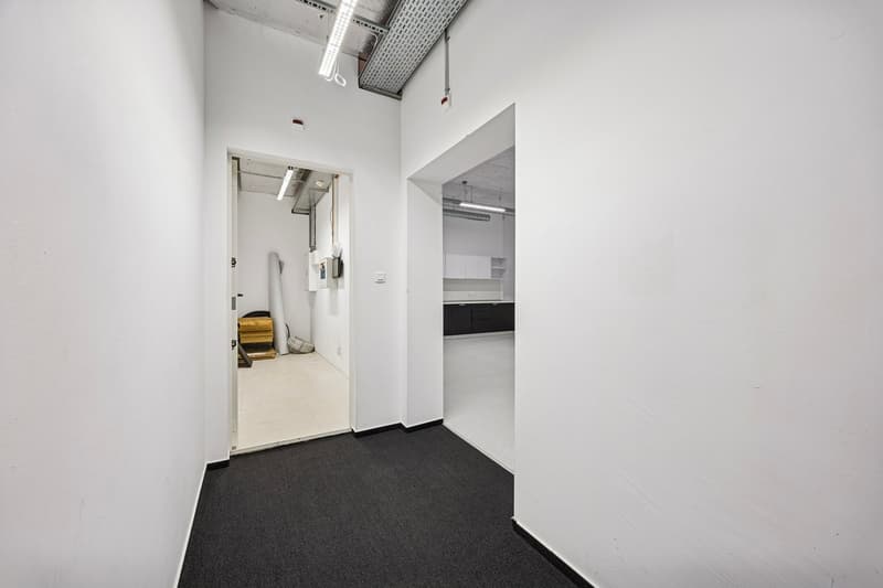 Empty corridor, white walls, white ceiling, black floor, ceiling lights, cabinets, and a counter are visible in the background.
