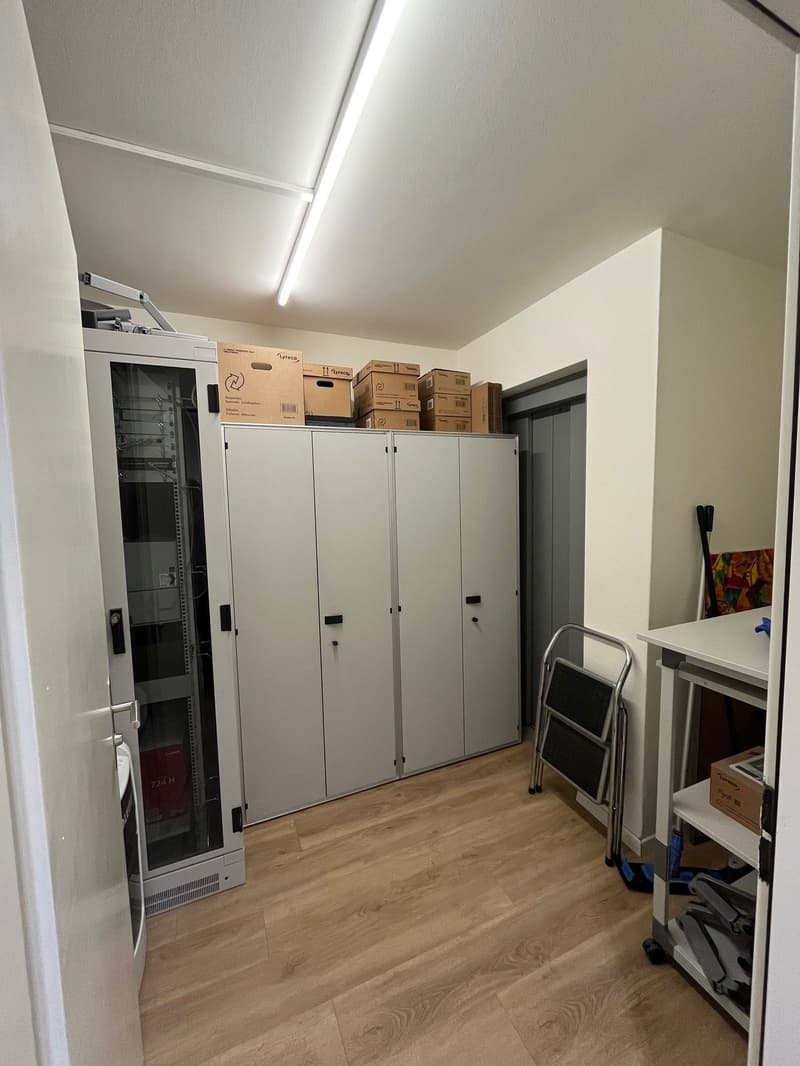 Storage room with wooden floor, white walls, cabinets, boxes, ladder, and a desk