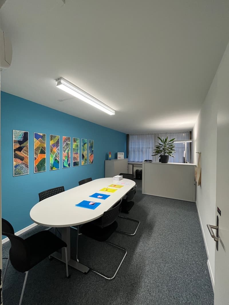 empty room, white table, black chairs, blue wall, paintings, white ceiling, fluorescent light, potted plant, white counter, white door
