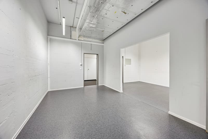 Empty room with white walls, gray floor, two doors, and ceiling lights