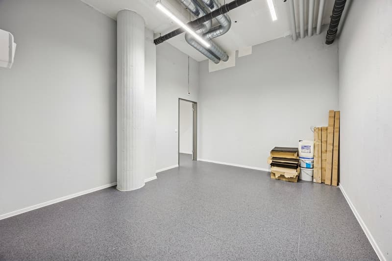 Empty room with gray floor, white walls, central pillar, and storage boxes on the right.