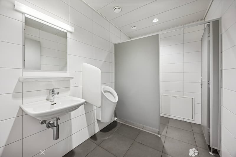 white tiled wall and floor, stainless steel urinal, white vanity sink with faucet, a mirror on the wall, a door