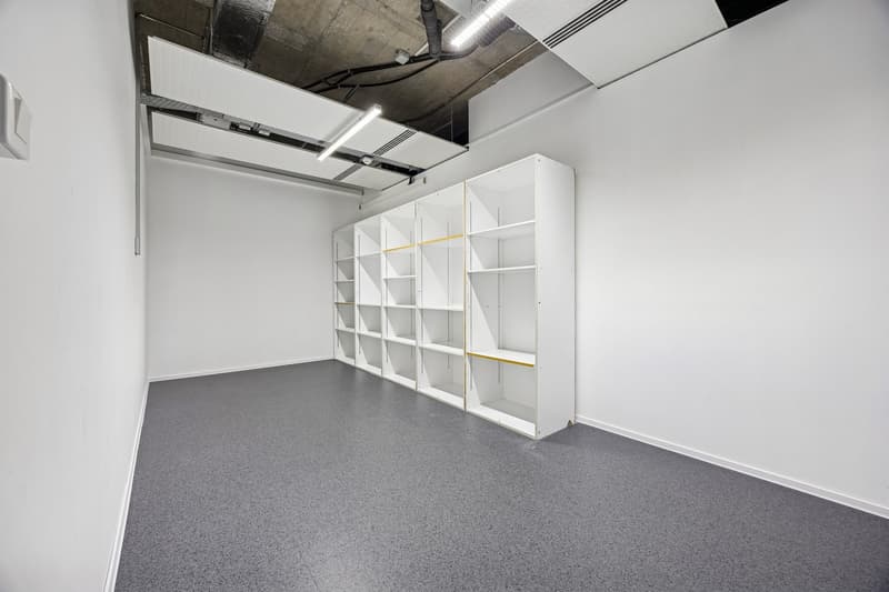 empty room with white walls, grey floor, ceiling with lights, tall white shelves with empty shelves