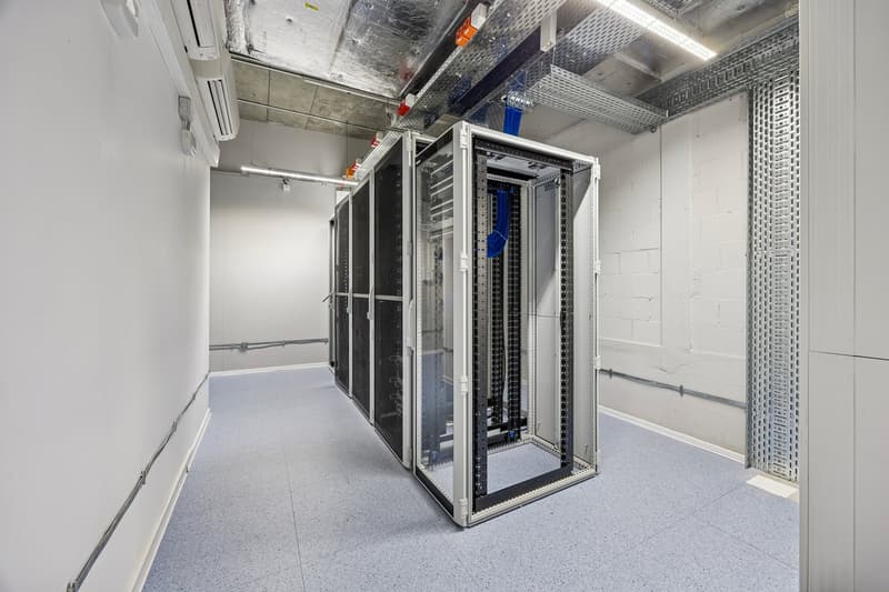 empty room, large server racks, gray floor, white walls, metal grates on the wall