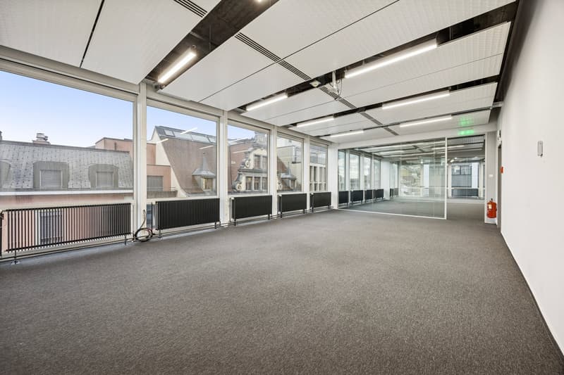 large windows, gray carpet, white walls, ceiling lights, fire extinguisher
