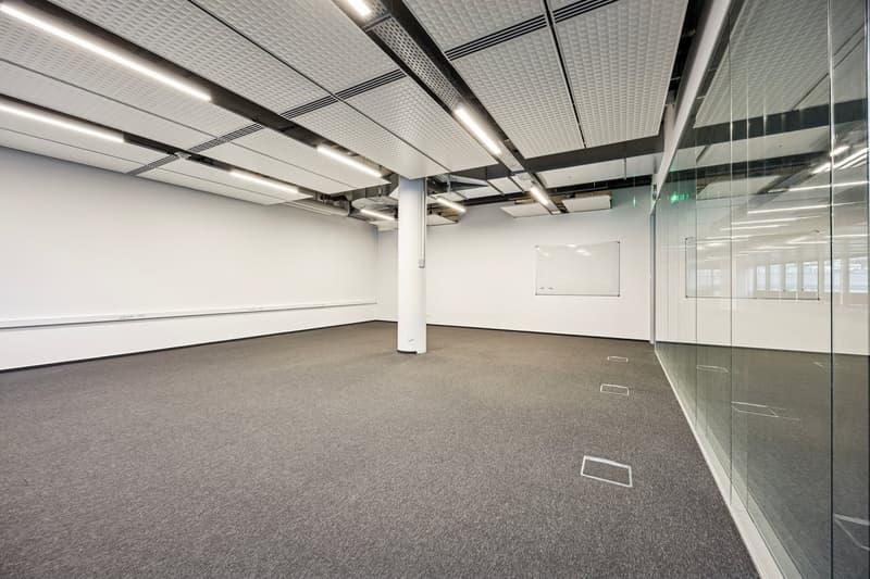 empty room with white walls, glass walls, gray carpeted floor, ceiling with panels and lights, whiteboard