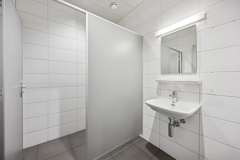 A small bathroom with white tiles, a sink, a mirror, and a shower area.