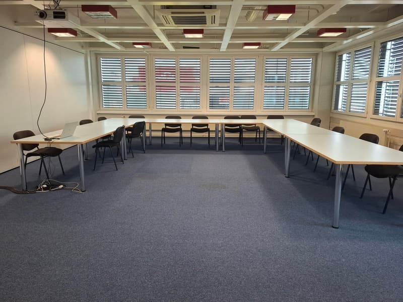 empty meeting room with long tables, closed windows, projector, ceiling lights