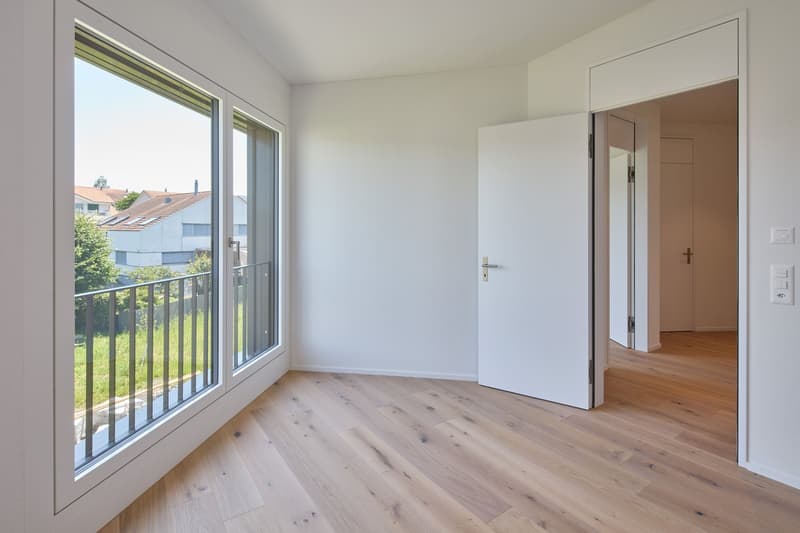 Empty room with wooden floor, white walls, large glass windows, and a balcony