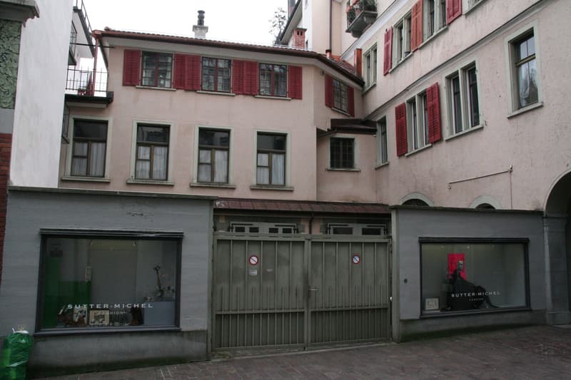 Old three story building, red shutters, brick walls, gated entrance, commercial storefronts