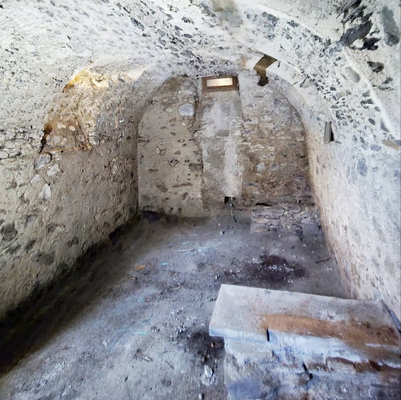 Small room with concrete floor, stone walls, and an arched passageway