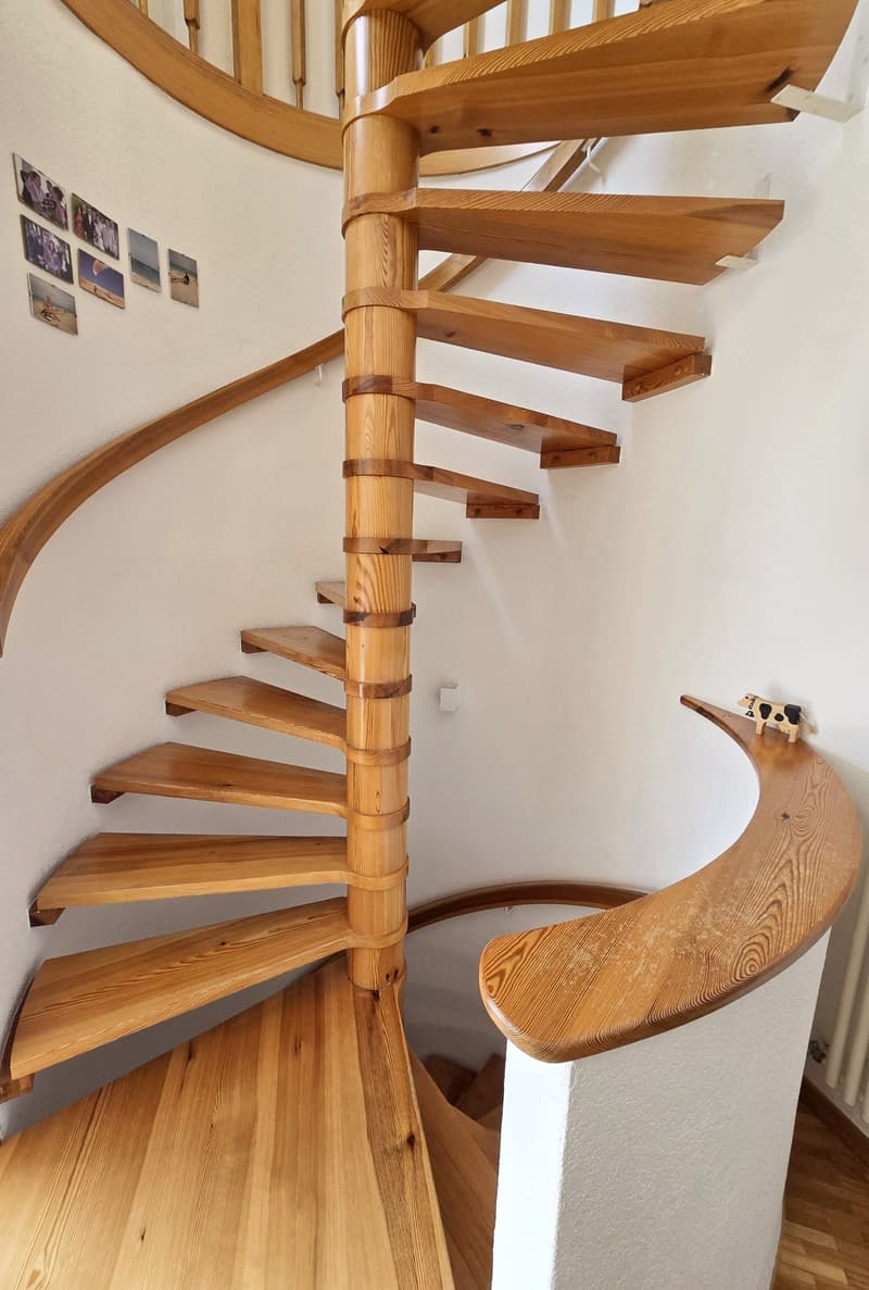 Wooden spiral staircase with handrail, pictures on the wall, wooden floor, white wall
