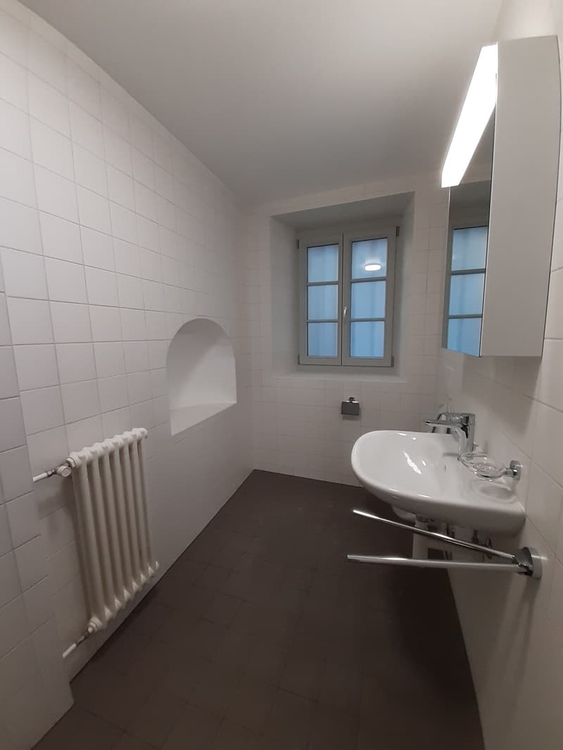 White tiled walls, tiled floor, white sink, mirror, white radiator, window