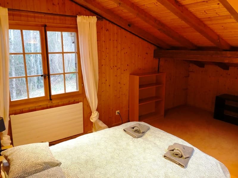 Cozy wooden cabin bedroom with large windows, wooden walls and ceiling, a fireplace, and a bed with towels on it