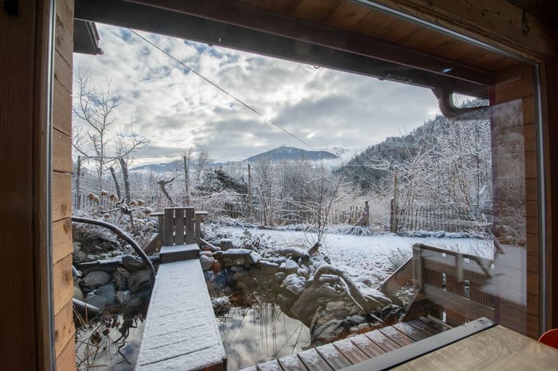 View of outdoor terrace, snow-covered ground, and mountains from a wooden house
