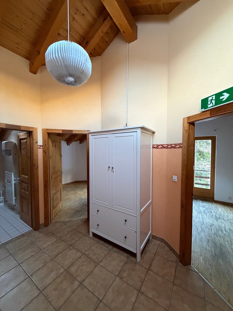 Empty room with wooden beam ceiling, white wardrobe, tile floor, wooden doors, emergency exit sign, power outlet