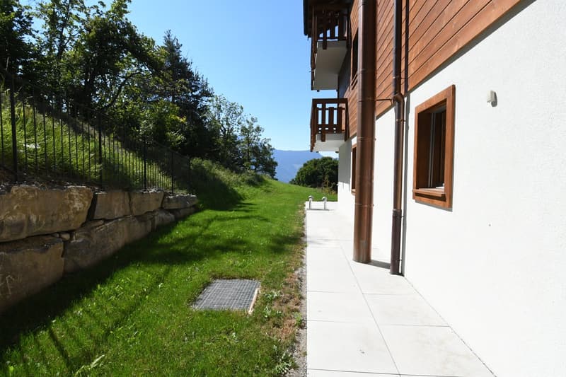 Apartment building with tiled pathway, balcony, white walls, stone wall, and green grass.