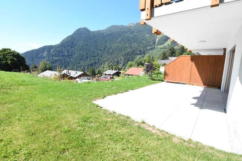 Apartment entrance with tiled floor, open gate, grassy hill, houses in the background, mountains