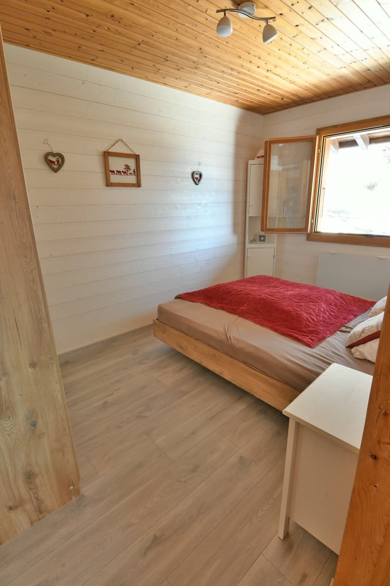 Wooden floor, white walls, wooden ceiling, bed, cabinet, bedspread, pillows, window, wall decorations