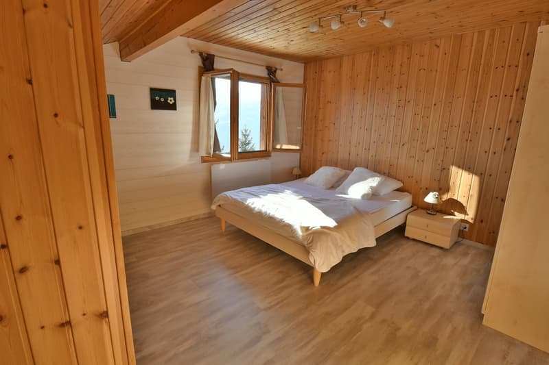 wood panel walls, wooden floor, double bed, white linens, 2 night lamps, nightstand with drawers, large window with shutters
