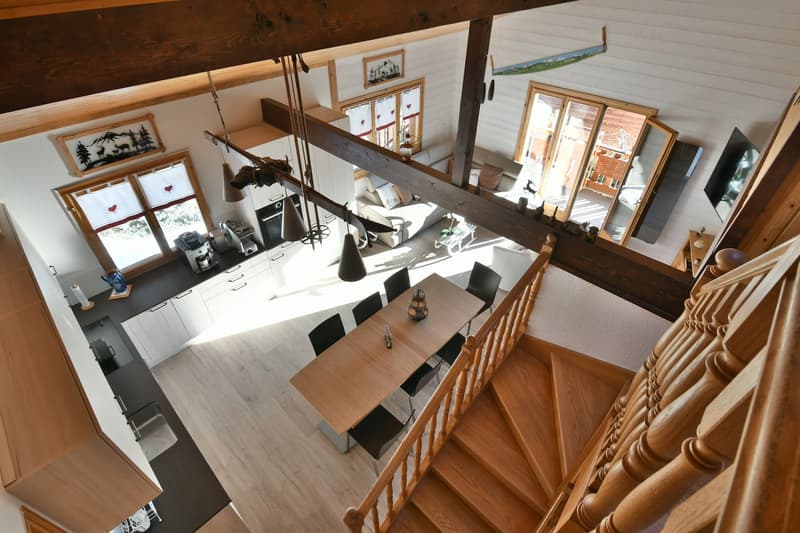 Open concept layout, wooden dining table, modern kitchen with granite countertop, modern staircase, wooden beams, cozy living area with sofa, glass windows, white walls
