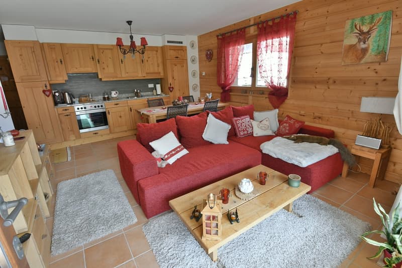 Cozy living room with wooden walls and cabinets, red sofa and loveseat, coffee table, kitchen area with stove and oven, chandelier lighting