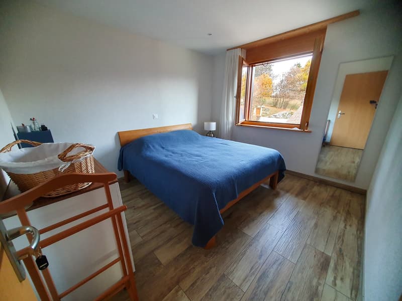 large bed, blue blanket, wooden side table with lamp, white wall, wicker basket on nightstand, full length mirror