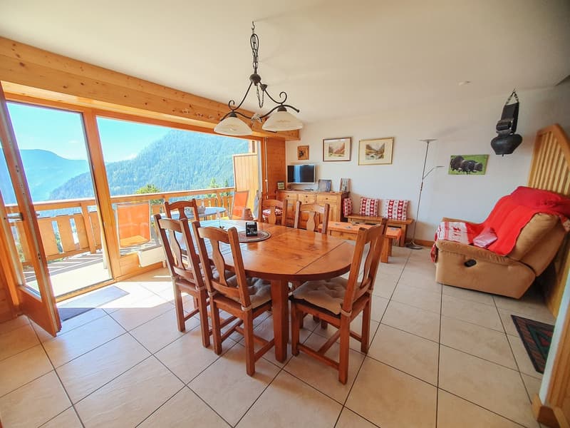 wooden table, chairs, open sliding glass doors leading to balcony, chandelier, white walls, white tiled floor, wooden ceiling, wooden shelves