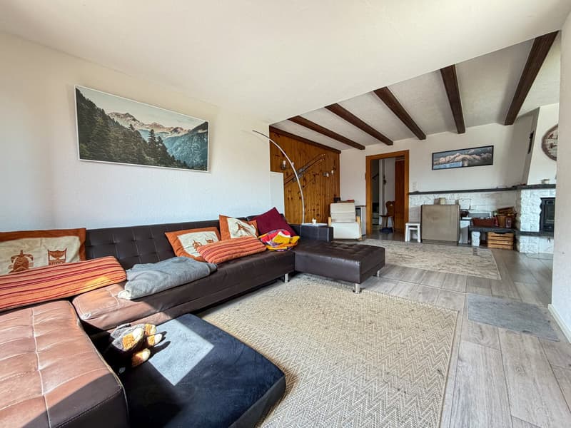 L-shaped sofa, wooden floor, fireplace, wooden beams, picture frames, rug, armchair, table, refrigerator