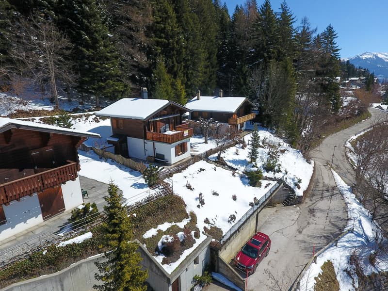 3 chalets, snow-covered ground, red car parked, wooden balconies, garage