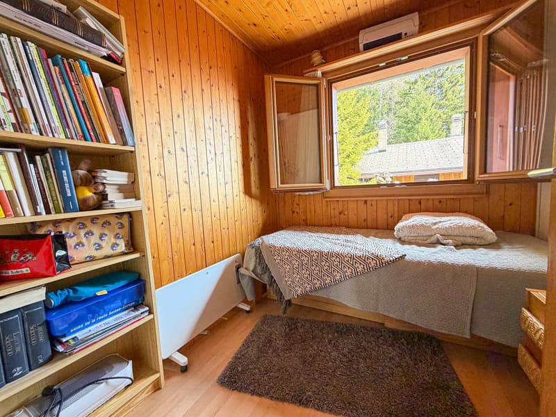 small room with bed, wooden walls, wooden floor, window with view, bookshelf, radiator