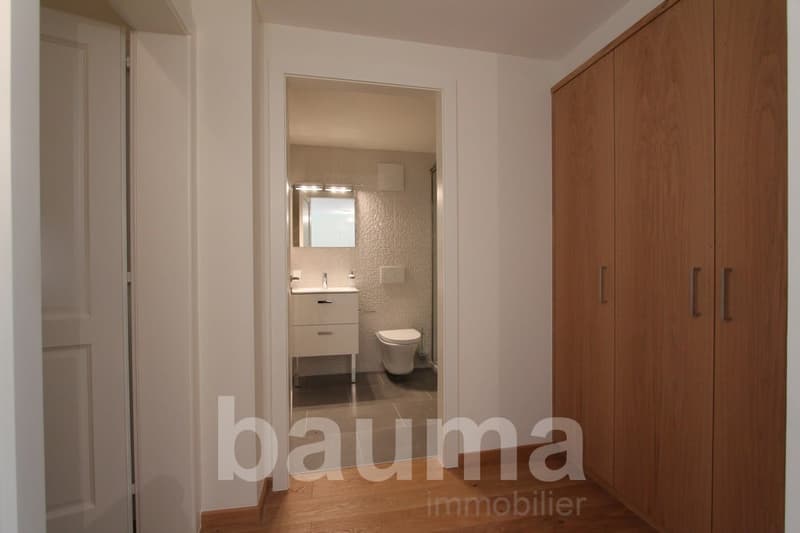 Spacious bedroom with wooden wardrobe, hardwood flooring, and an ensuite bathroom visible through the open doorway.