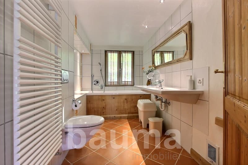 modern bathroom with bathtub, large mirror, white tile, toilet, sink, and wooden door