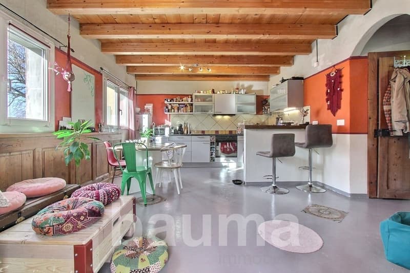 Open plan kitchen and dining area, 3 high stools, dining table, seating area with bench, plant, pillows, wooden beams, and exposed ceiling