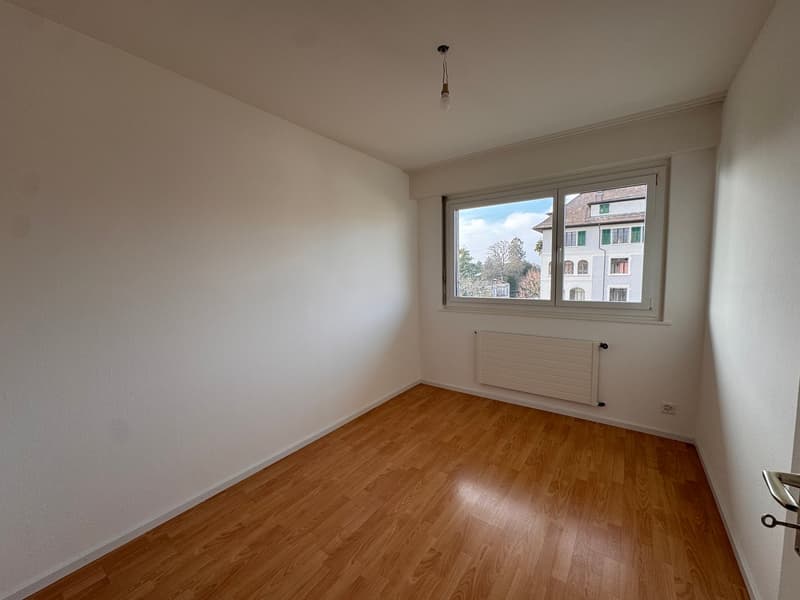 empty room with white walls, wooden floor, window with view, radiator