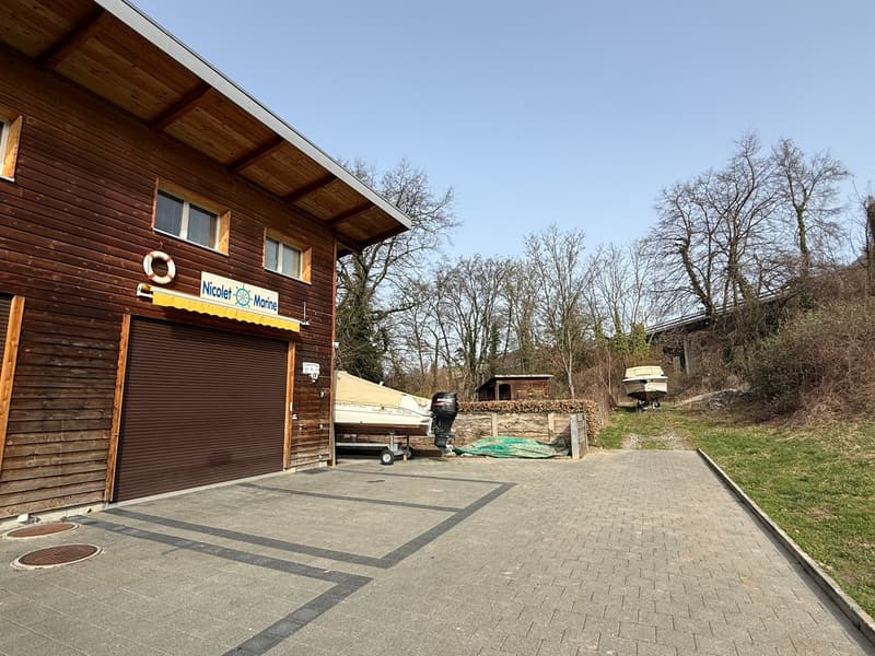 wooden building with a garage, a lifebuoy above the garage door, a boat with a motor outside, paved driveway