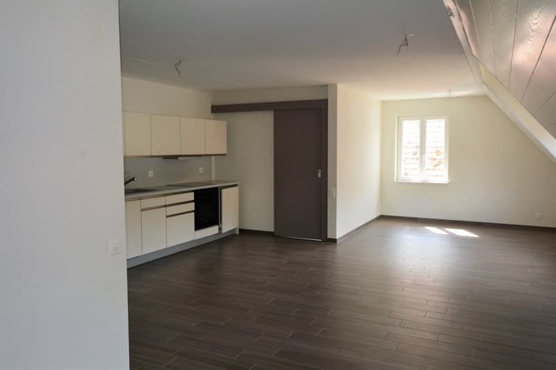 Open-concept studio apartment with kitchen area, hardwood-style flooring, and a window providing natural light.