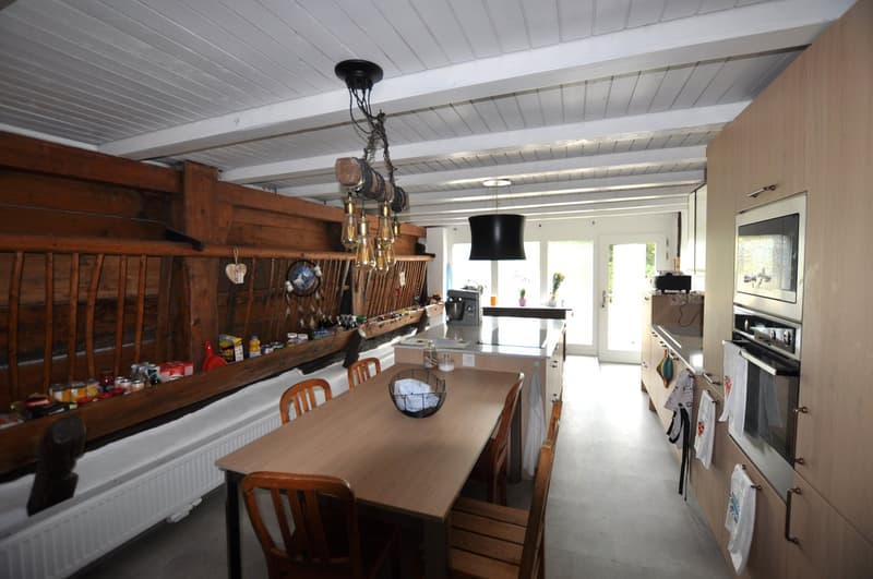 Rustic kitchen with wooden beams, dining table, kitchen appliances, and various kitchen items on the shelves.