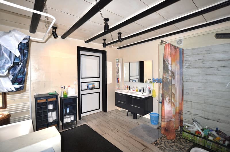 The image shows a bathroom with a vanity cabinet, a mirror, and various bathroom accessories. The room has a rustic, industrial-style decor with exposed beams on the ceiling and a tiled floor. There is a dishwasher visible in the image.