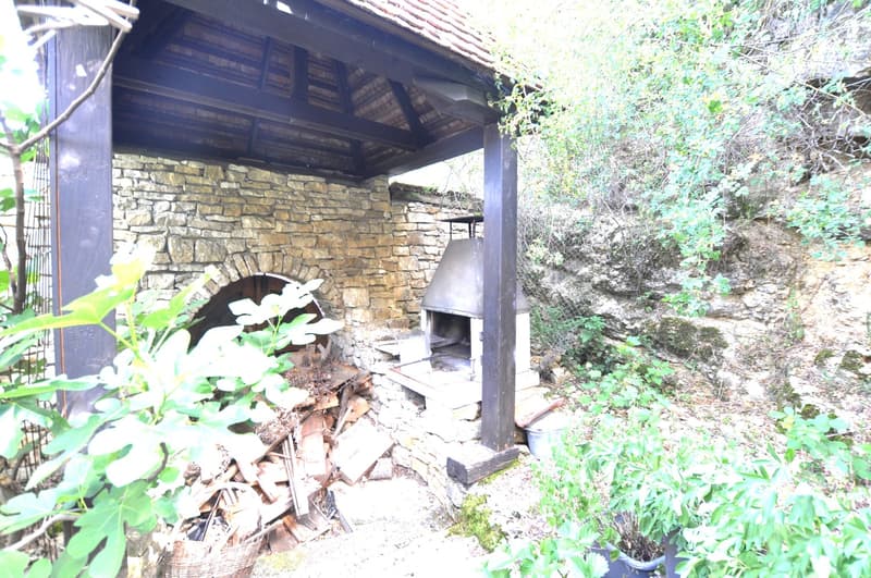 Stone and wood structure with an arched entrance, a fireplace, and a tiled roof surrounded by lush greenery
