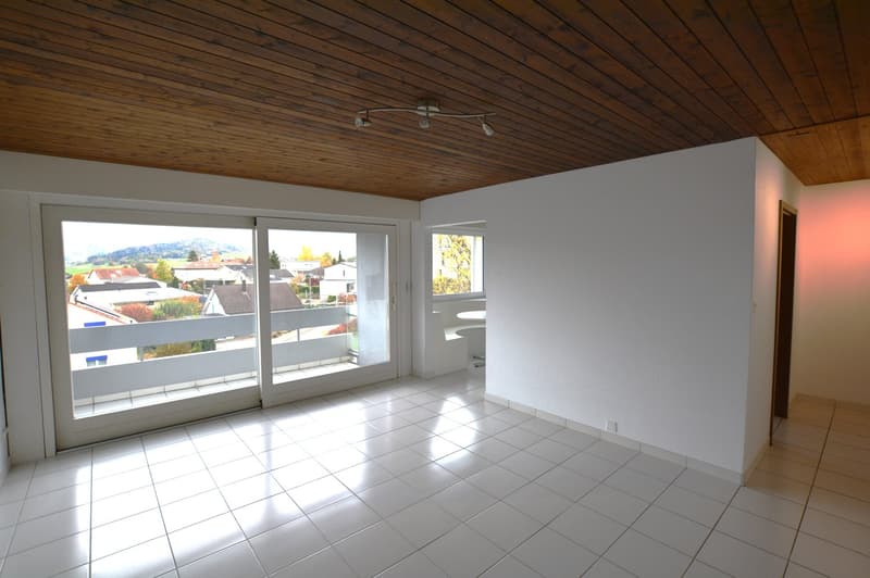 Room has wooden ceiling, large sliding glass doors, tiled floor, balcony, and view of a cityscape