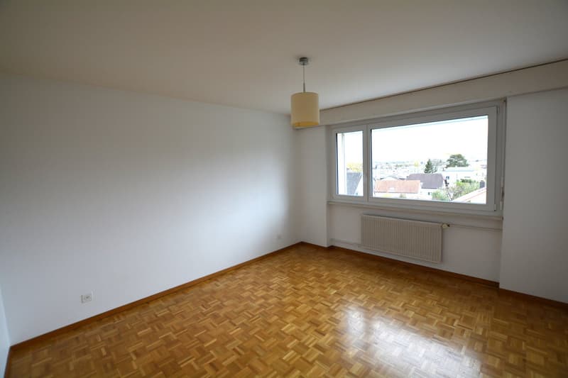 Empty room with white walls, wooden floor, and a window with a city view