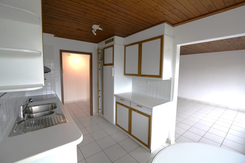 An empty kitchen with white tiled floor, white walls, wooden cabinets, double sink, and light fixtures.