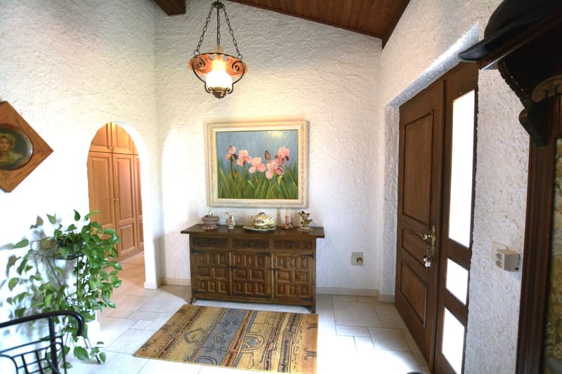 An arched doorway, wooden cabinet, decorative items on a side table, and a potted plant in the corner.