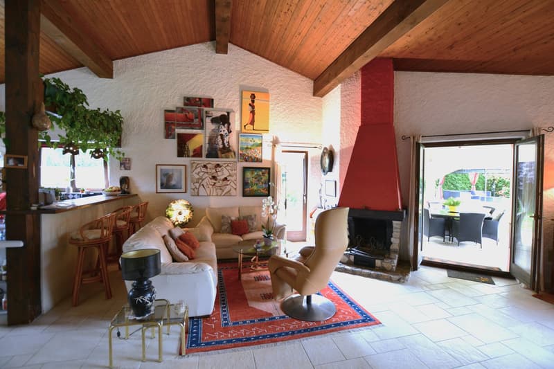 fireplace, sofa, chairs, rug, coffee table, table lamp, artwork, kitchen counter, wooden ceiling, white tiles
