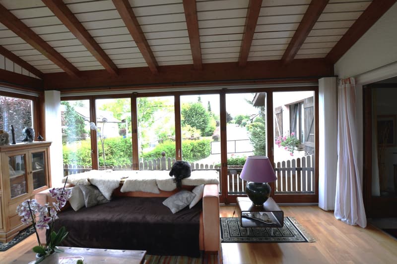 wood floor, wooden beams, couch with furs, flowers, side table with lamp, glass windows