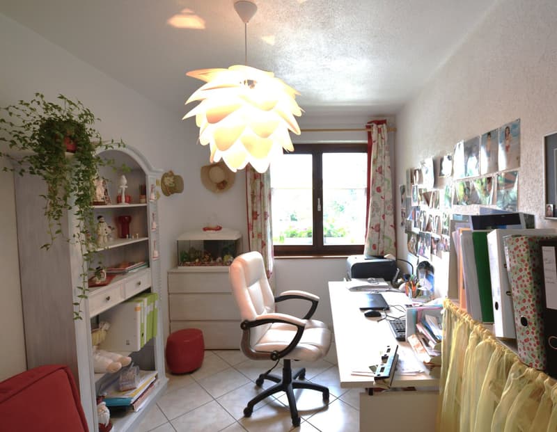 An office room with a desk, chair, cabinet, window, and various decorative items.